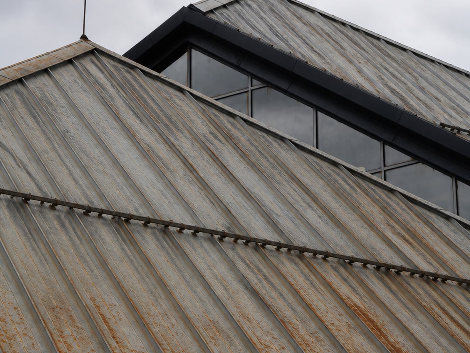 Same roof planes before metal installation — oxidized panels and rust along the seams