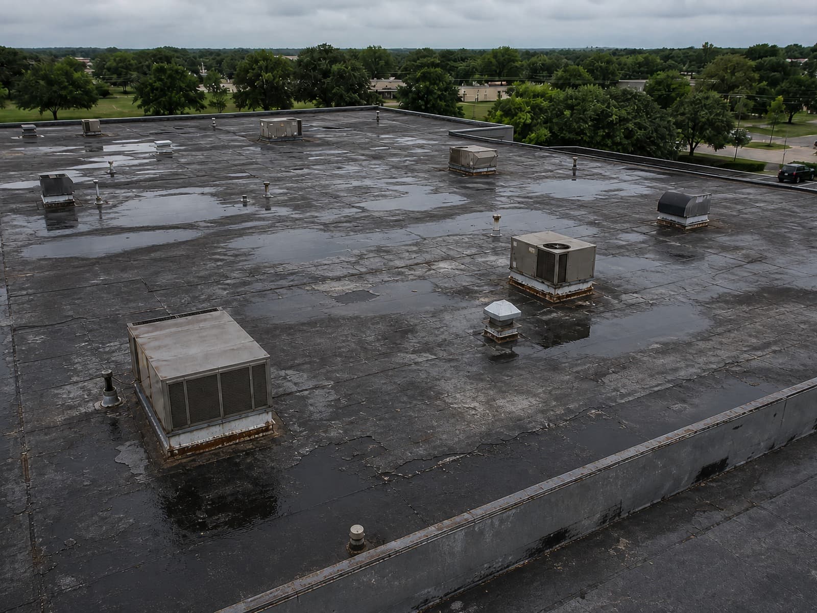 Same commercial rooftop before replacement — ponding water, failed membrane, and rusted flashing
