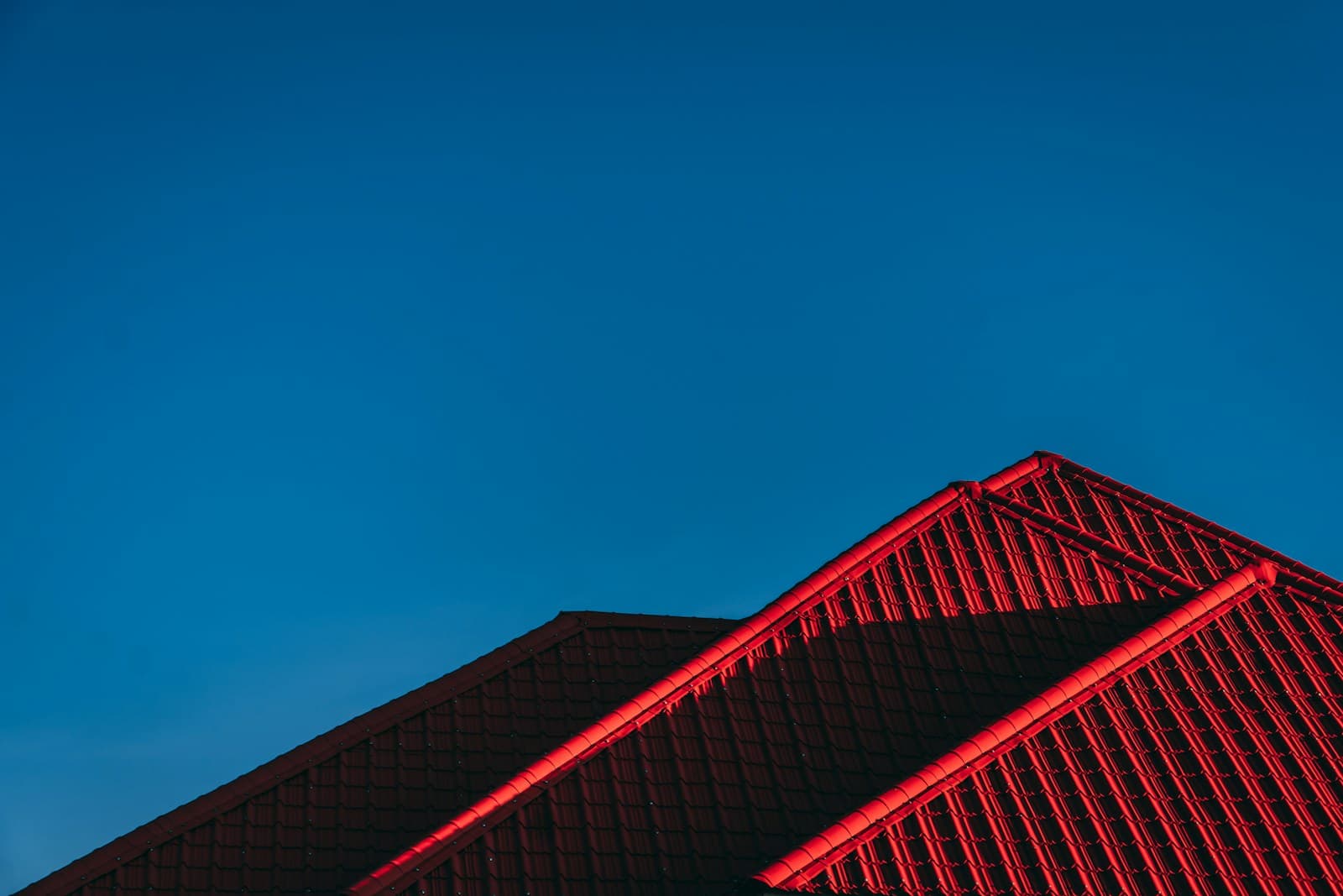 Residential red tile roof peaks against deep blue sky